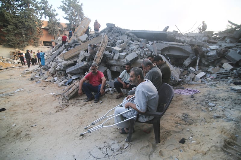 Palestinians sit by a building destroyed in an Israeli air strike in Rafah, Gaza. AP