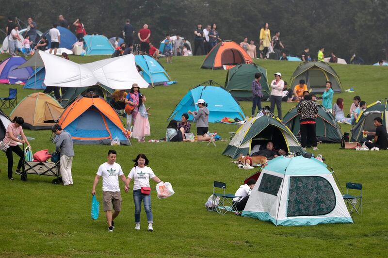 A couple walk by people setting camps on a scenic mountain in Yanqing, on outskirts of Beijing on Sunday, Aug. 30, 2020. China currently has more than 200 people being treated in hospital for COVID-19, with another more than 300 in isolation after testing positive for the virus without displaying symptoms. (AP Photo/Andy Wong)