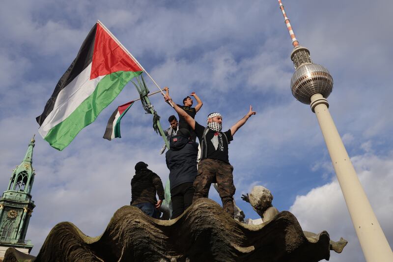 A man waves a Palestinian flag from atop Neptune Fountain during a "Freedom for Palestine" protest at Alexanderplatz in Berlin. Getty Images