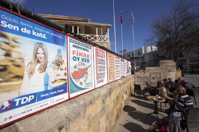 People sit next to campaign posters for parliamentary elections at a cafe in the northern part of Nicosia in the self-proclaimed Turkish Republic of Northern Cyprus (TRNC) which is only recognized by Turkey, on January 3, 2018. / AFP PHOTO / Birol BEBEK