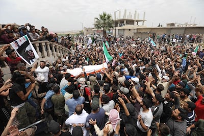 TOPSHOT - A picture taken on June 9, 2019 shows Syrians waving rebel flags and portraits of Abdel-Basset al-Sarout during the funeral of the late rebel fighter in al-Dana in Syria's jihadist-controlled Idlib region, near the border with Turkey. The Syrian goalkeeper turned rebel fighter who starred in an award-winning documentary died on June 8 of wounds sustained fighting regime forces in northwestern Syria, his faction said. Sarout, 27, was among dozens of fighters killed since June 6 in clashes with regime forces on the edges of the Idlib region. / AFP / OMAR HAJ KADOUR
