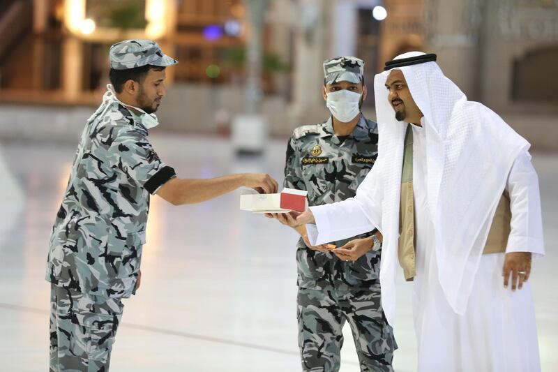 A worshipper offers sweets to a security guards, some with face masks, during Eid Al Fitr prayers at the Grand Mosque. AFP