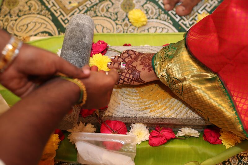 The groom makes offerings of flowers as the bride steps on a stone as part of the marriage ceremony