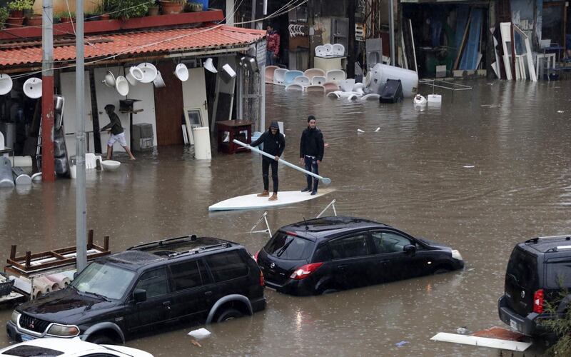 Lebanese men use a paddle board as means of transportation on a flooded road due to heavy rain, at the southern entrance of the capital Beirut. AFP