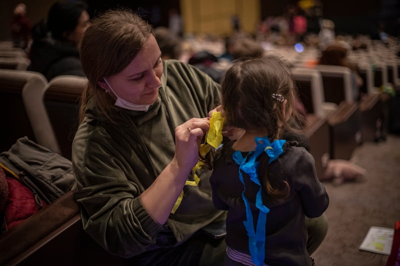 A woman ties ribbons in Ukrainian national flag colours in a girl's hair as people wait at a refugee assistance centre in Prague, Czech Republic. EPA