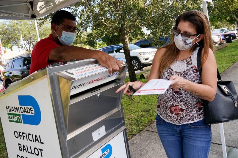 Carlos Amado, left, with the Miami-Dade Supervisor of Elections, helps Isabel Lui drop off her ballot in North Miami. AP Photo