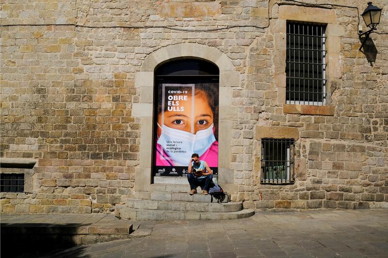 A man reads a book next to a poster reading "COVID-19, open your Eyes" in Barcelona, Spain. Reuters