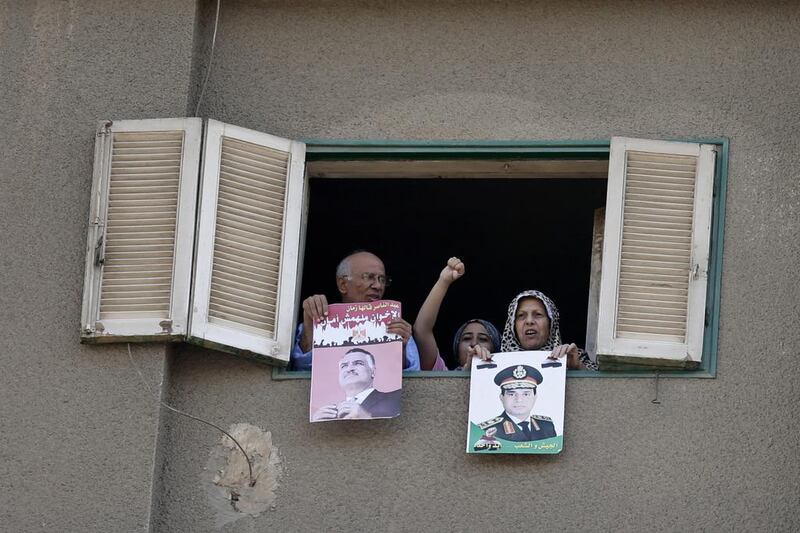 Residents of Cairo hold out posters of the late president Gamal Abdel Nasser, left, and the current military chief, Gen Abdel Fattah El Sisi, while watching a protest by supporters of the Muslim Brotherhood last Friday. Hassan Ammar / AP Photo