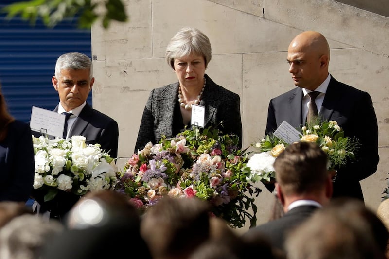 British Prime Minister Theresa May, London mayor Sadiq Khan, left, and British Home Secretary Sajid Javid stand on stage to observe a minute's silence and lay flowers on London Bridge to mark the one year anniversary of the attack that happened there, in London, Sunday, June 3, 2018. Britain's resolve to "stand firm" against terrorism is stronger than ever, Prime Minister Theresa May said Sunday, a year since a deadly vehicle-and-knife attack on London Bridge. Eight people were killed and almost 50 injured when three Islamic State group-inspired attackers ran down pedestrians on the bridge, then stabbed people at bars and restaurants in nearby Borough Market. (AP Photo/Matt Dunham)
