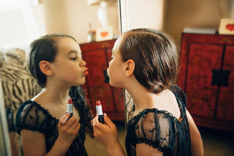 Mixed race girl applying lipstick in mirror. Getty Images