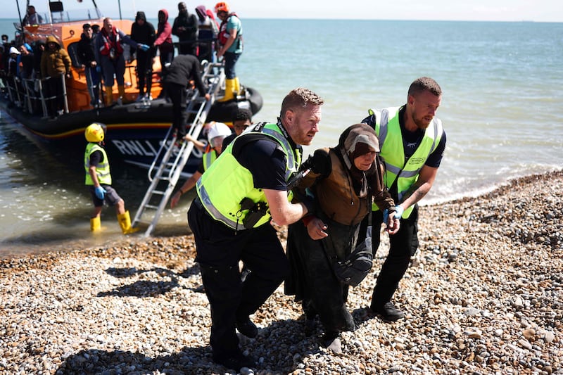 Officials helping a woman off a lifeboat and across the beach at Dungeness. AFP
