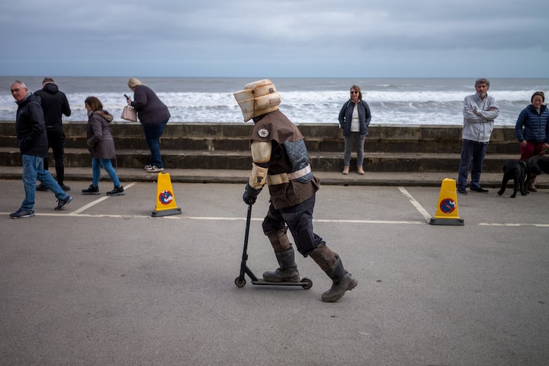 A man dressed as a character from Star Wars rides a scooter along the seafront