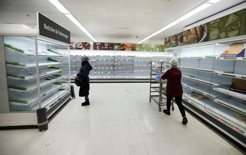 A Sainsbury's worker walks past a customer next to empty shelves at a Sainsbury's store in Harpenden, southern England. Reuters