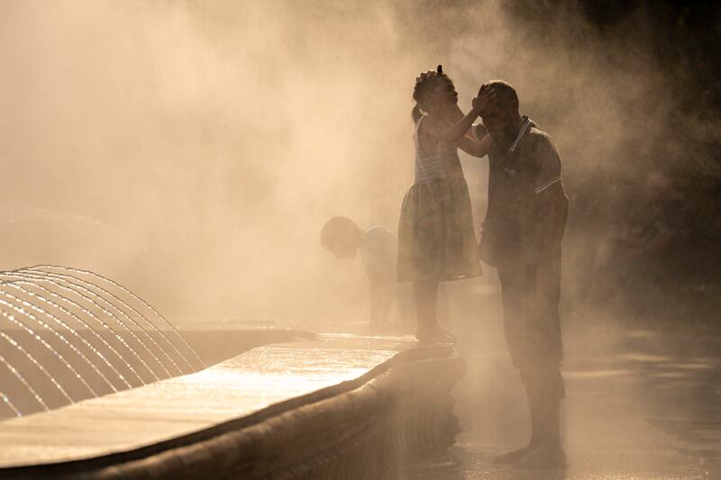 A father and daughter are shrouded by mist from a public fountain in Bucharest, Romania. AP