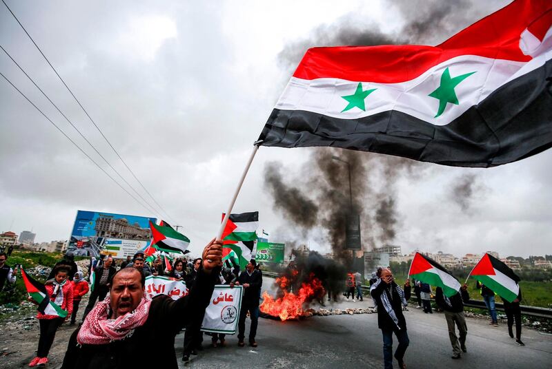 A man waves a Syrian national flag as others wave Palestinian flags behind him while marching during a demonstration. AFP