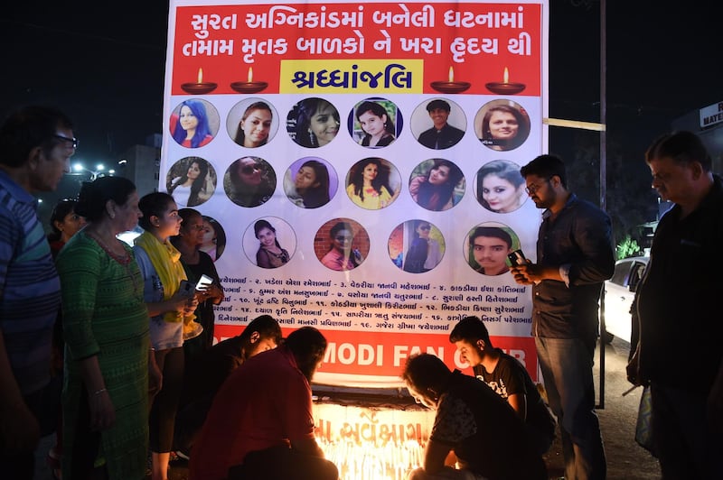 Members of a Narendra Modi fan club place candles next to o banner with pictures of victims of yesterday's fire in a building housing a college in Surat, during a candlelight vigil in Ahmedabad on May 25, 2019. At least 19 students -- most of them female -- died on May 24 in a fire at an Indian building housing a college, officials said, as images showed people jumping to escape the blaze. "The students lost their life both because of the fire and jumping out of the building," Deepak Sapthaley, a fire official in the western city of Surat, told AFP.
 / AFP / SAM PANTHAKY
