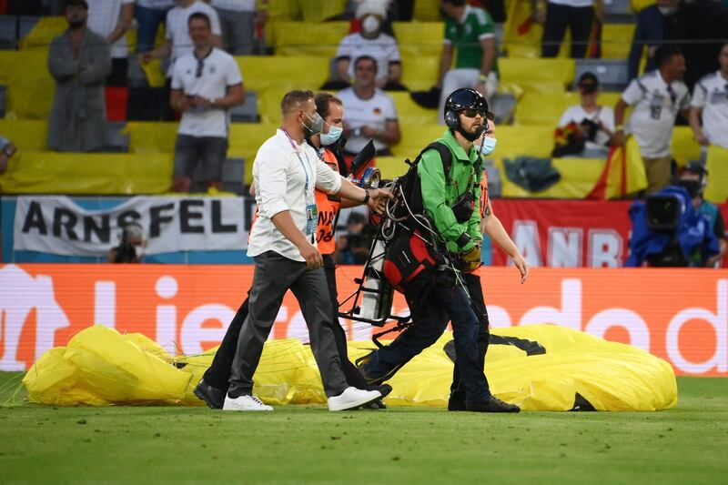 The  paraglider is escorted off the pitch by security. AFP