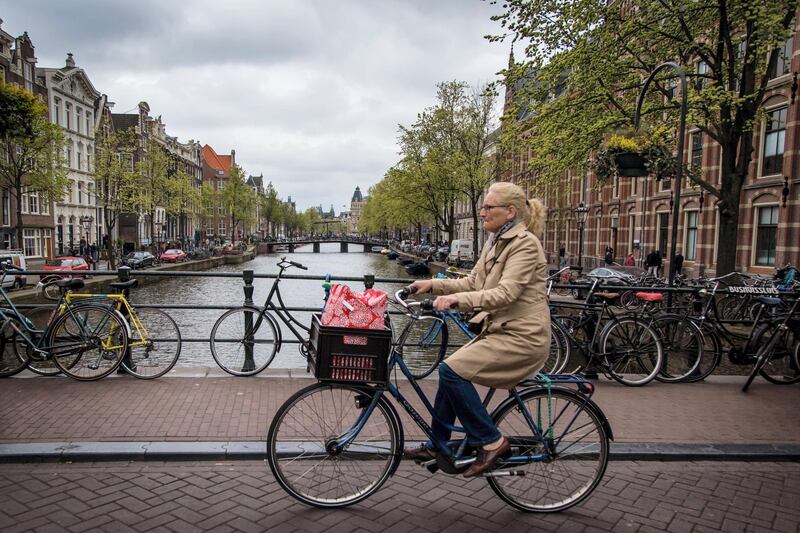 View of a canal in Amsterdam with a woman on a bicycle on April 12, 2017. / AFP PHOTO / Aurore Belot