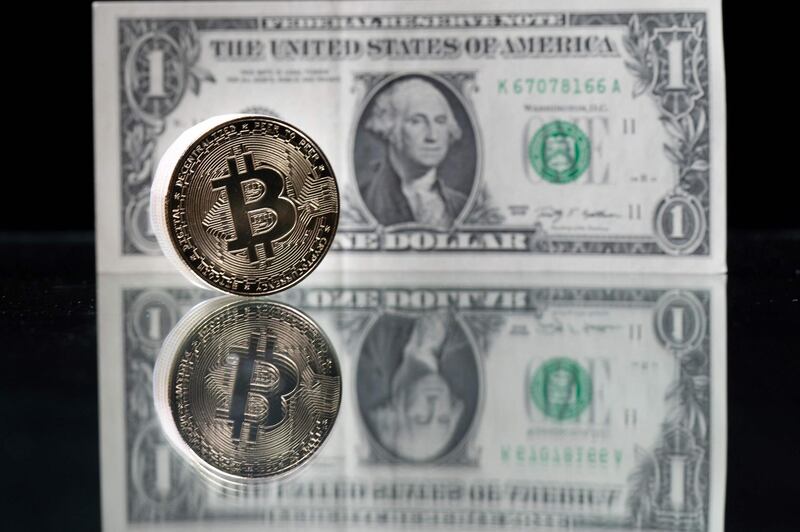 This photograph taken on April 26, 2021 in Paris shows a physical imitation of the Bitcoin crypto currency pictured with a US one dollar bank note. / AFP / Martin BUREAU
