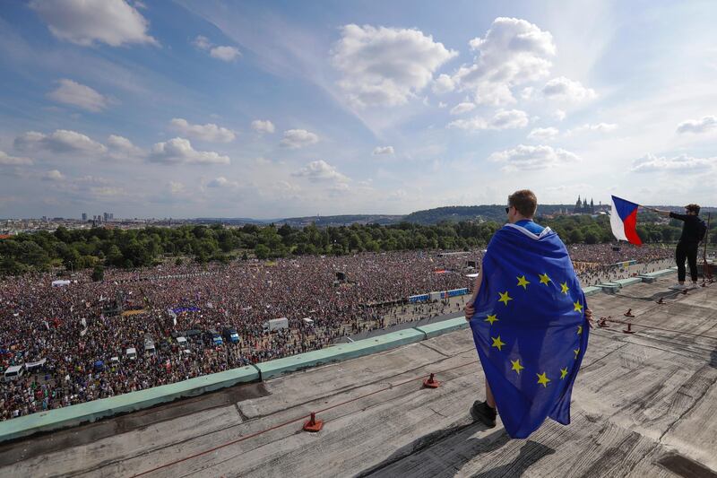 A man wrapped in in an European Union flag watches protesters gather in Prague, Czech Republic. AP