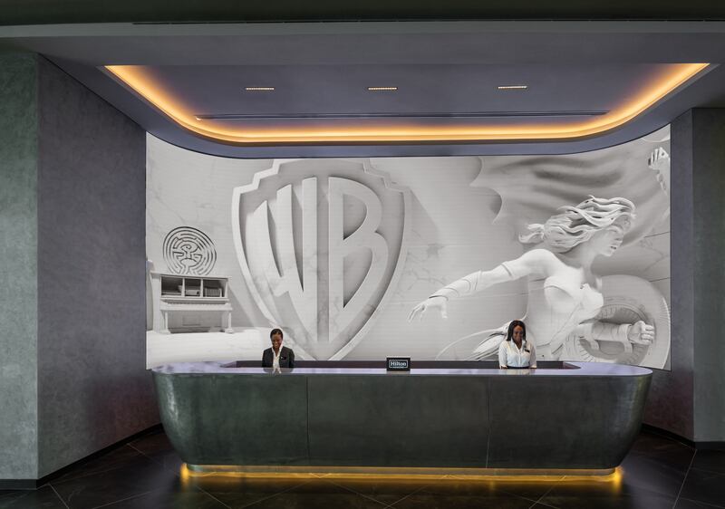 The check-in desk is backed by a sculpted marble-like wall panel showing scenes from the entertainment company's history. Photo: Hilton 
