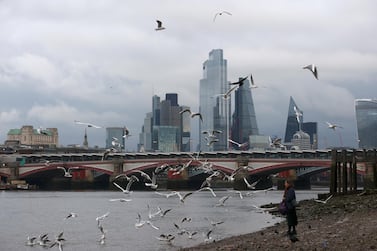 A woman feeds birds on the bank of the river Thames with London's financial district seen in the background. While the UK economy has now grown for six months running, it still remains 7.9% below pre-pandemic levels. Reuters