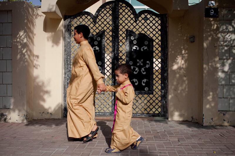 Sharjah, United Arab Emirates - June 23 2013 - (L-R) Mohammad Al Jabri holds hands with his brother Abdulrahman Al Jabri, 2, as they visit homes in their neighborhood. They are participating in Hag El Leila, an Emirati tradition that occurs every year 15 days before the start of the month of Ramadan. The tradition involves children walking from door-to-door singing and collecting sweets and money. (Razan Alzayani / The National)  FOR RYM GHAZAL STORY  *** Local Caption ***  RA0623_hag_el_layla_008.jpg