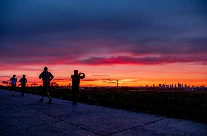 A man takes a picture of the skyline as other people run by in Frankfurt, Germany. AP Photo