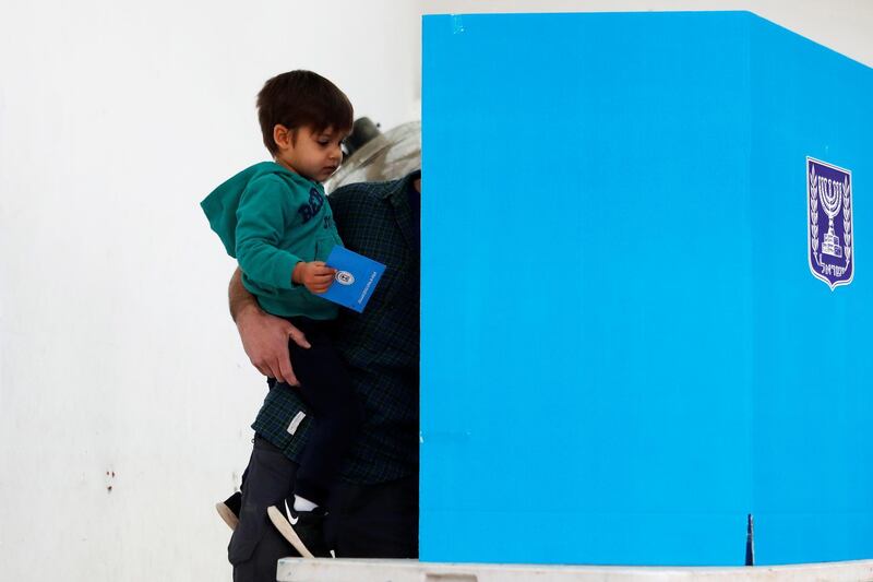 A boy watches his father as he stands behind a booth at a polling station and votes in Israel's national election, in the Israeli settlement of Nokdim, in the occupied West Bank. Reuters