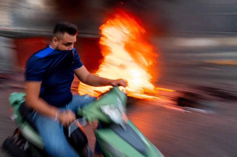 A man on his scooter passes next to garbage containers and tires that were set on fire by anti-government protesters to block the main road in Beirut, Lebanon. Protesters closed several major roads in the Lebanese capital amid rising anger as the currency hit a new record low on the black market, electricity cuts increased and the government raised the price of bread for the first time in more than a decade. AP Photo