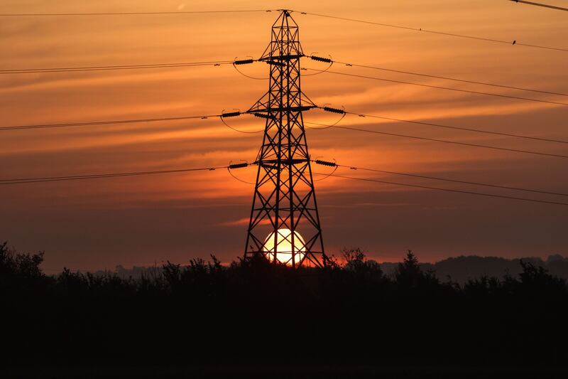 The sun rises behind an electricity transmission tower in the UK. Bloomberg