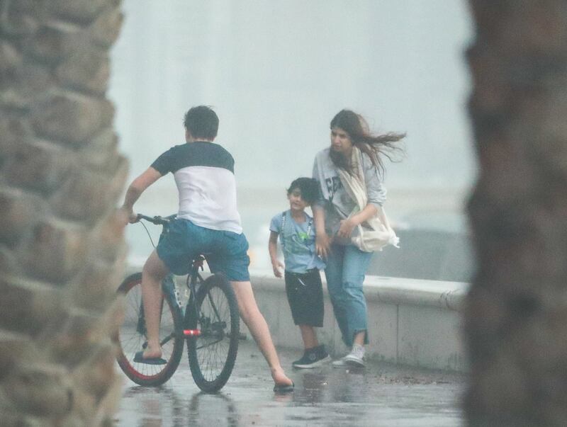 Walkers are caught out by sudden strong winds and rain on the corniche in Sharjah. Victor Besa / The National