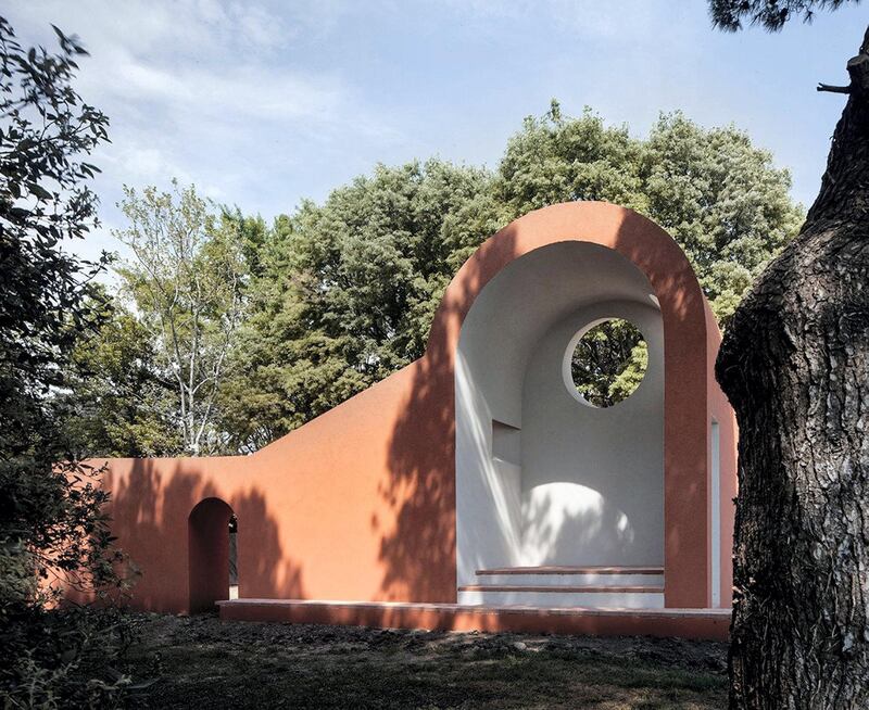 With gentle curves and walls of a warm terra cottta hue, is the chapel of Ricardo Flores and Eva Prats of Spain. The structure has an enclosed area with a vaulted ceiling several steps above ground level, and a door that offers an escape into the woods beyond.