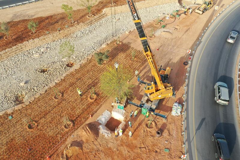 An aerial picture shows workers using a crane to plant trees in a park project by the roadside in the Saudi capital Riyadh, on March 29, 2021. - Although the OPEC kingpin seems an unlikely champion of clean energy, the "Saudi Green Initiative" aims to reduce emissions by generating half of its energy from renewables by 2030. (Photo by - / AFP)
