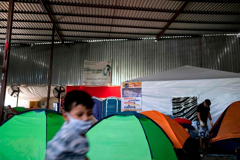An asylum seeker stands next to a tent for COVID-19 suspects (background) as a child plays, at the Juventud 2000 migrant shelter in Tijuana, Baja California state, Mexico.  Thousands of asylum seekers wait in Mexico for the US Departments of Justice and Homeland Security to resume the migration hearings after they were suspended due to the COVID-19 pandemic. The World Refugee Day is commemorated on June 20.  AFP