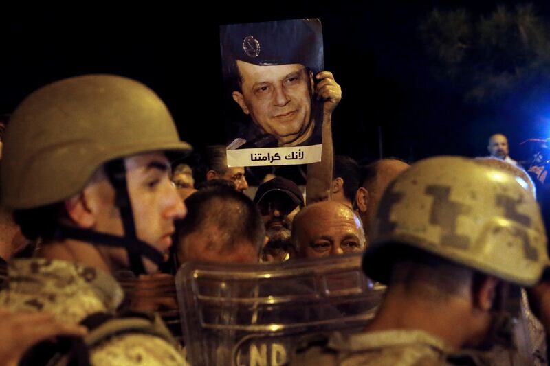 A supporter of Lebanese President Michel Aoun holds up his picture with Arabic that read "Because you are our dignity," as Lebanese republican guards stand guard during a protest near the presidential palace in the Beirut suburb of Baabda, Lebanon. AP Photo