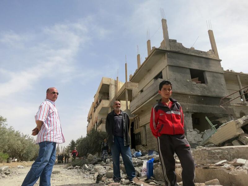 Syrians stand in front of heavily damaged buildings on April 8, 2016 in Al Qaryatain, a few days after Syrian regime forces seized it from ISIL. AFP / Max DELANY

