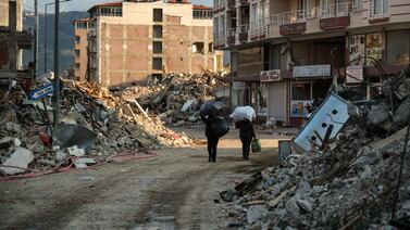 Women carry their belongings as they walk past collapsed buildings in Samandag, Turkey, on Thursday. Getty