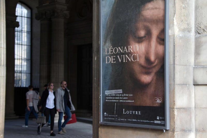 Visitors walk near a poster for the exhibition 'Leonardo da Vinci' at the Louvre Museum in Paris.  AFP