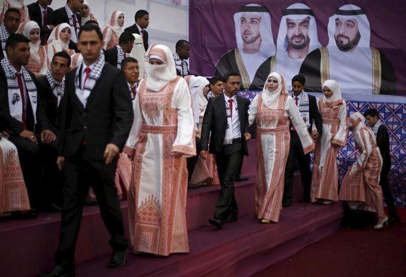 Palestinian grooms walk with their brides on the stage alongside a photo showing President Sheikh Khalifa, Sheikh Mohammed bin Zayed, Crown Prince of Abu Dhabi and Deputy Supreme Commander of the Armed Forces, and Sheikh Mansour bin Zayed. Mohammed Salem / Reuters