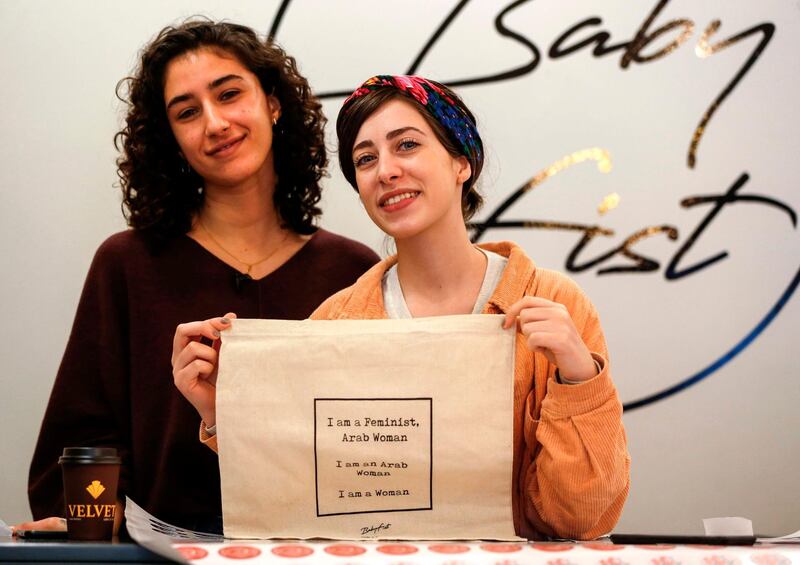 Palestinian fashion designer and label founder Yasmeen Mjalli (L), along with her creative director Amira Khader, pose for a picture with one of their label "BabyFist's" canvas bags in their shop in Ramallah in the occupied West Bank on December 19, 2018. It's only three words on a T-shirt or embroidered on a denim jacket, but they carry a powerful message: "Not you habibti (darling)." "BabyFist" label founder Yasmeen Mjalli, 22, sees the clothes helping to empower Palestinian women facing unwelcome male attention in public, placing on the fabrics of muted colours and on canvas bags messages in English and Arabic inside drawings of flowers and other designs. / AFP / ABBAS MOMANI
