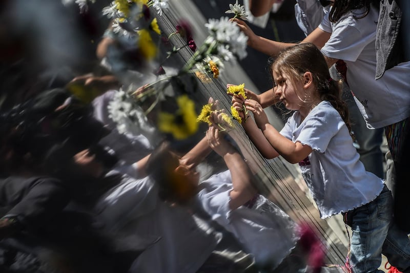 Relatives place flowers on a memorial wall in tribute to the victims of late Colombian drug lord Pablo Escobar, before the inauguration of the 'Inflection Park' in Medellin, on December 20, 2019. - The park was build on the same ground of the demolished Monaco building, which was once home to Escobar. (Photo by JOAQUIN SARMIENTO / AFP)