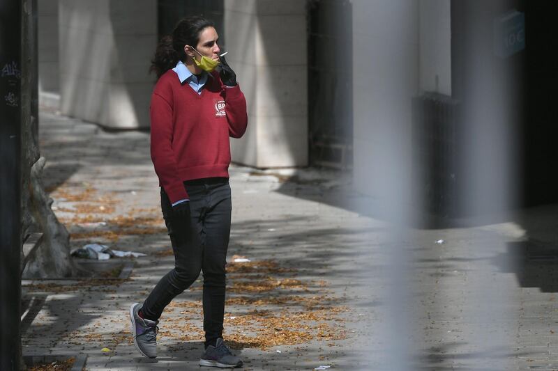 A woman wearing a face mask smokes a cigarette in Vilanova i la Geltru near Barcelona on March 24, 2020 amid a national lockdown to stop the spread of the COVID-19 coronavirus. Spain is Europe's second-hardest hit country by the coronavirus outbreak, with over 33,000 confirmed cases of the disease and 2,182 deaths. / AFP / LLUIS GENE
