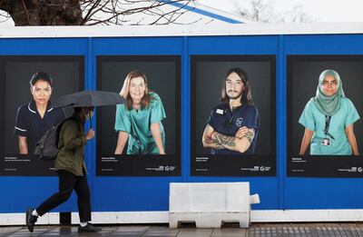A person walks past images of NHS workers displayed on hoardings outside a temporary field hospital at St George's Hospital in London. Reuters