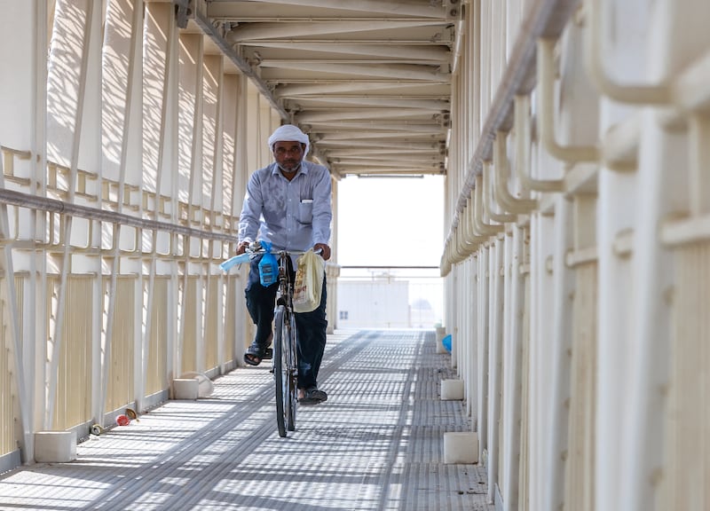 A man on his bike crosses a road overpass in the sunshine. 