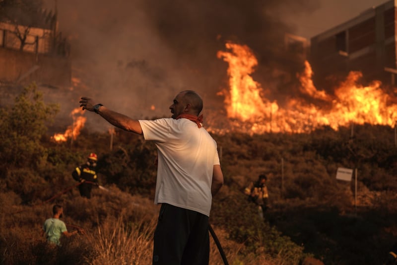 Firefighters and volunteers work to extinguish a burning field during a wildfire in Saronida, south of Athens. Bloomberg