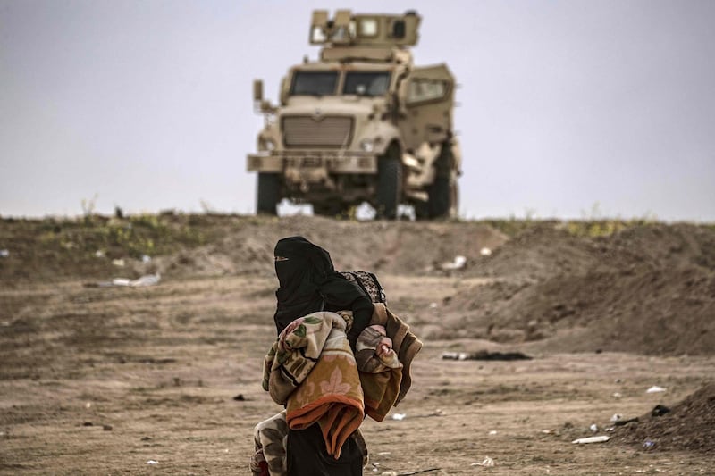 A Syrian woman walks past a military vehicle as hundreds of civilians, who streamed out of the Islamic State group's last Syrian stronghold, headed towards a screening point for new arrivals run by US-backed Syrian Democratic Forces outside Baghouz in the eastern Syrian Deir Ezzor province on March 5, 2019. Shell-shocked and dishevelled, hundreds of women and children stumbled through eastern Syria's windswept desert carrying what little they could after fleeing the IS group's final speck of territory. / AFP / Delil SOULEIMAN
