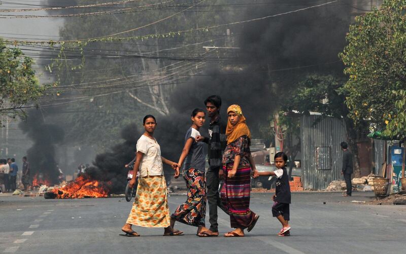 People walk on a street as barricades burn behind them in Mandalay. reuters