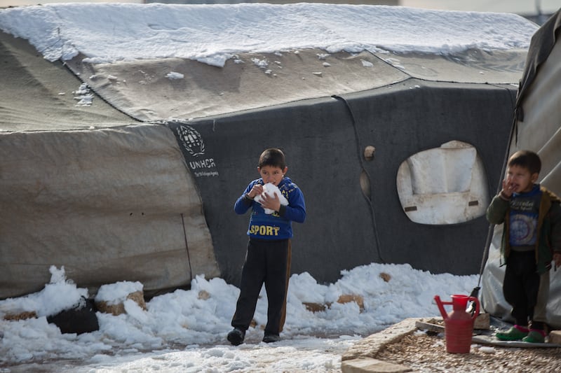 A displaced Syrian child walks near his tent and eats the snow that fell on the camp.