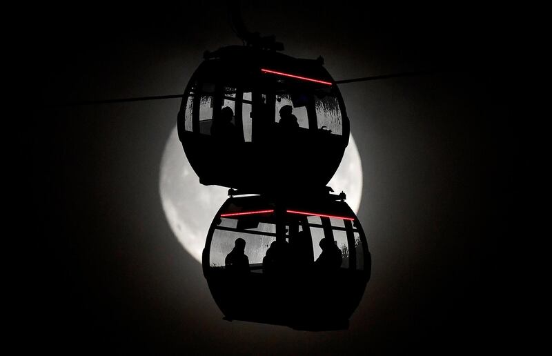 Passengers are seen silhouetted by the moon as they ride on the Emirates Air Line cable car over the River Thames in London, Britain.  Reuters